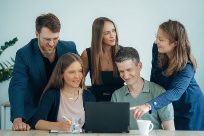 Fünf HMS-Mitarbeitende arbeiten gemeinsam an einer Lösung und besprechen Inhalte an einem Laptop.